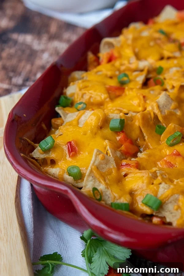 A close-up shot of a Mexican chicken rice casserole, showcasing melted cheese, visible chicken pieces, and crunchy tortilla chips on top.