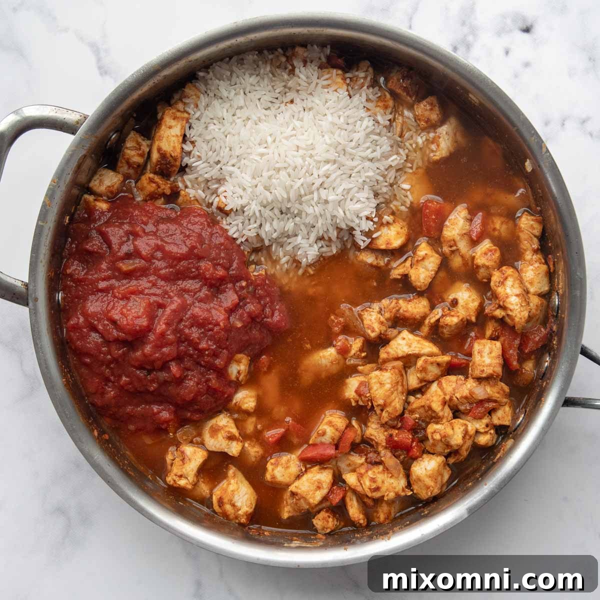 Broth being added to the rice and chicken mixture in a skillet, showcasing the liquid ingredients before simmering.