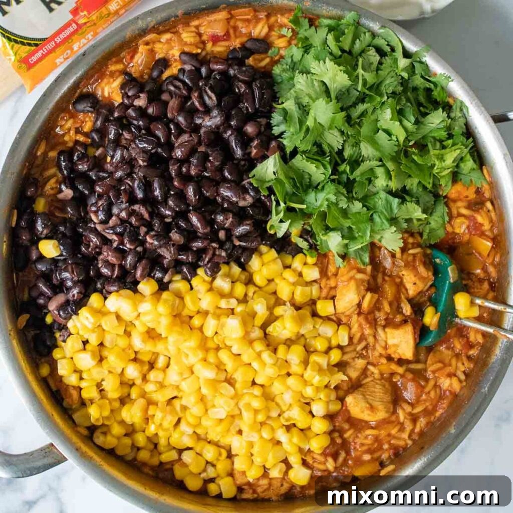 The cooked chicken and rice mixture being stirred in a saucepan, with black beans, sour cream, and cilantro added, ready for layering.