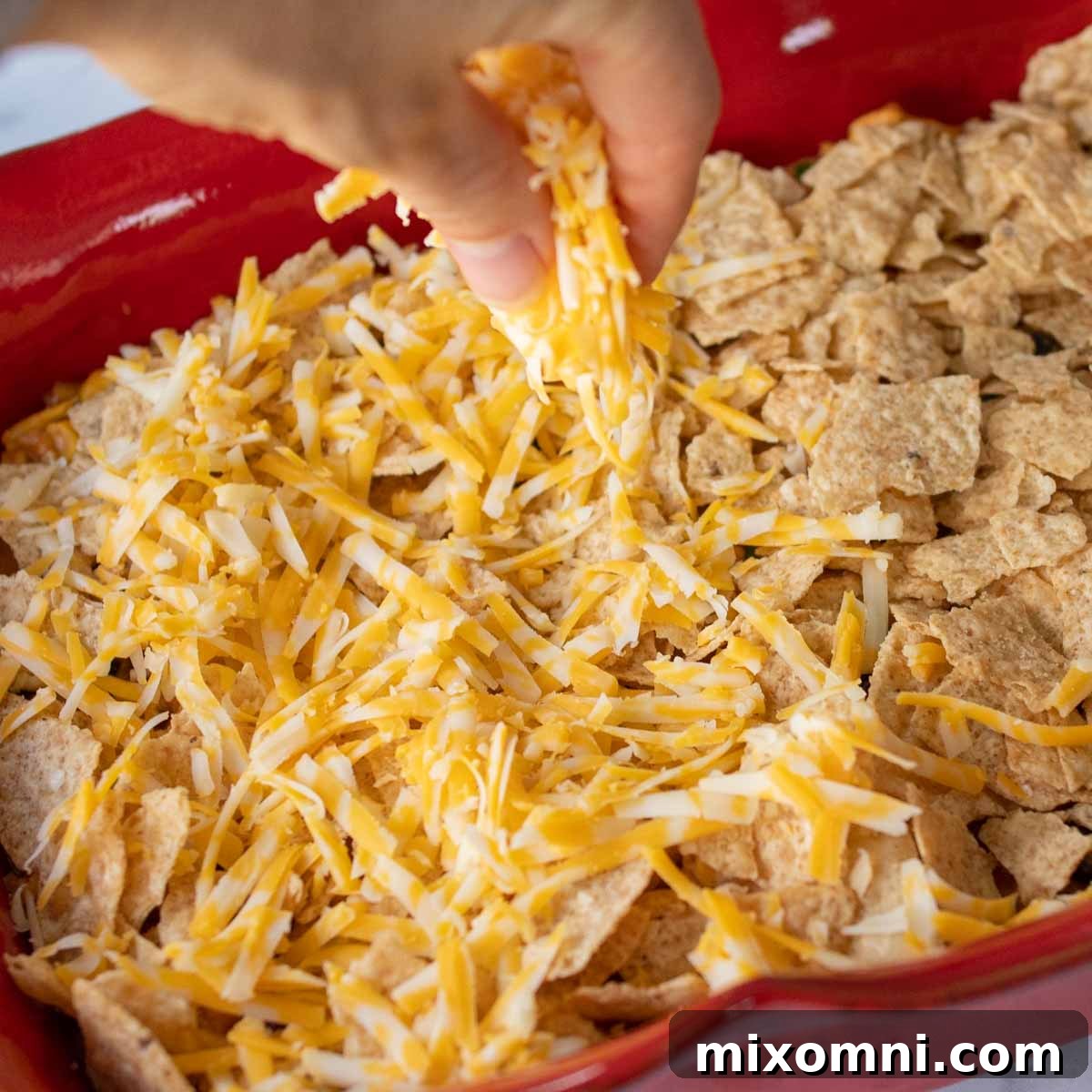 Shredded cheese generously sprinkled over a layer of tortilla chips in a baking dish, preparing for the oven.
