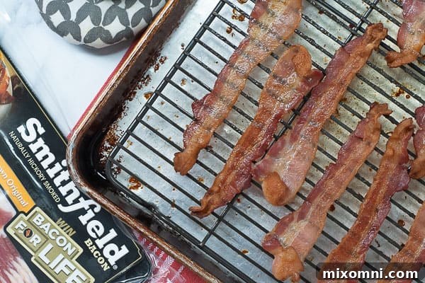 Crispy, perfectly cooked bacon strips laid out on a baking sheet, ready to be chopped and added to recipes or enjoyed on their own. The even cooking indicates the effectiveness of the oven method.
