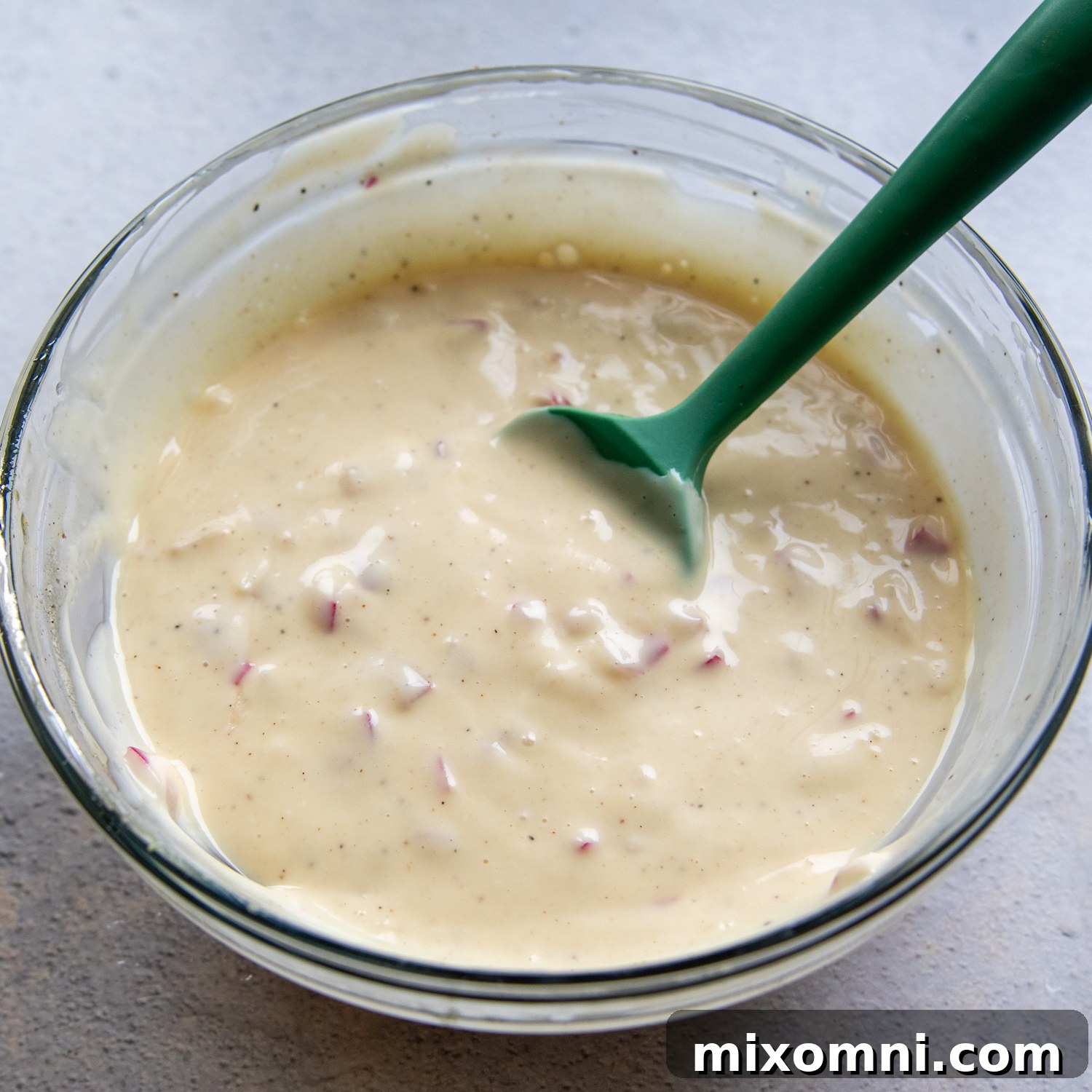 Salad dressing in a glass bowl with a green spoon, ready to mix.