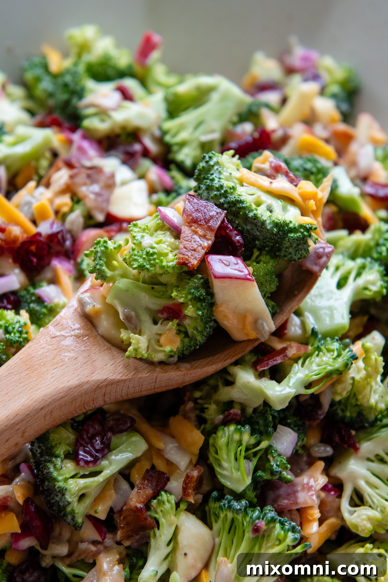Broccoli salad on a wooden spoon above a bowl of salad, ready to be served.