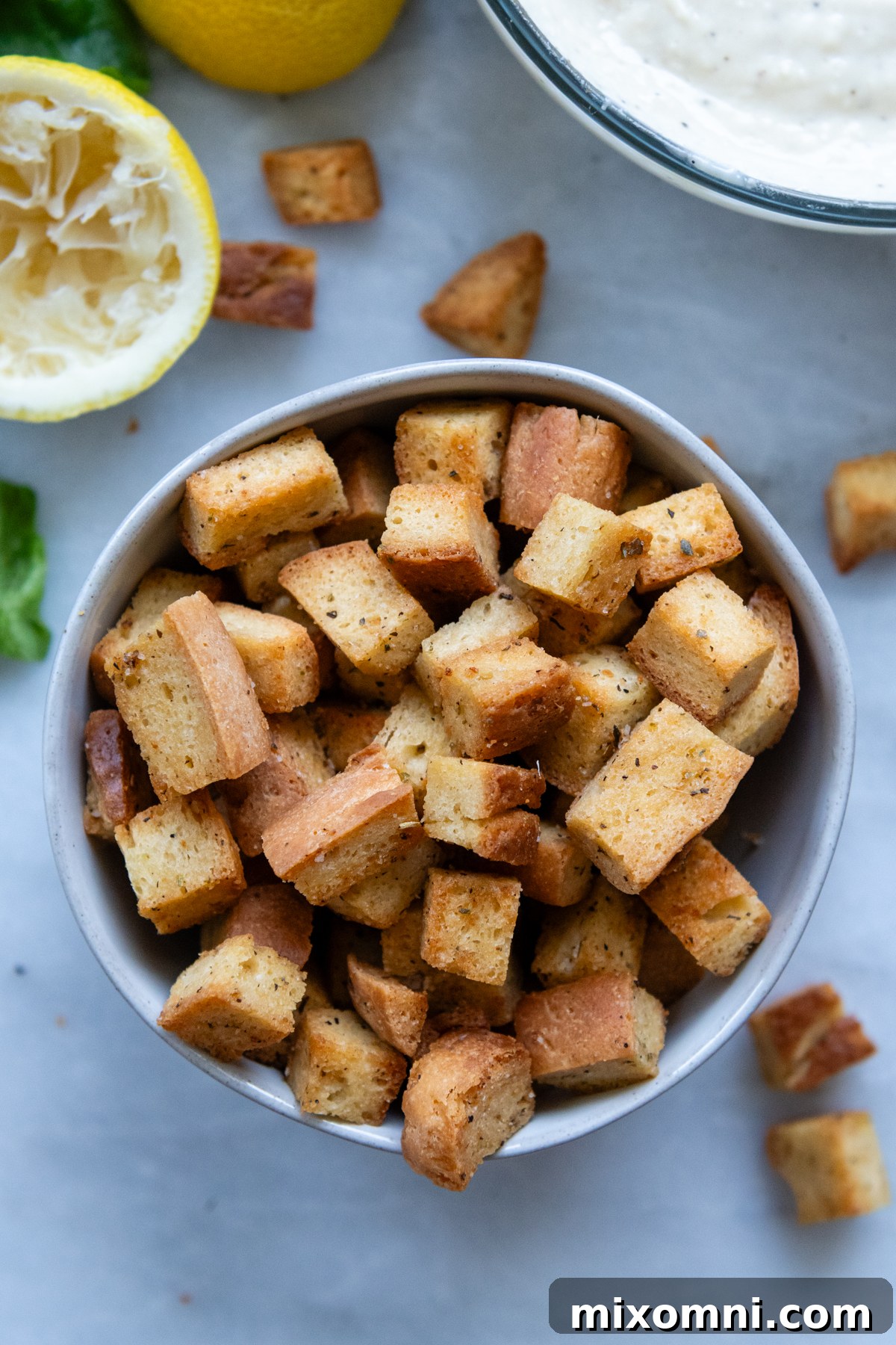 Overhead shot of a rustic bowl brimming with golden, homemade gluten-free croutons, garnished with fresh herbs.