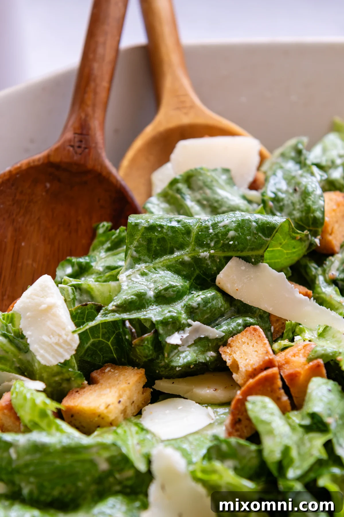 A beautifully tossed Caesar salad in a large bowl, showcasing crisp romaine, creamy dressing, parmesan, and crunchy croutons.