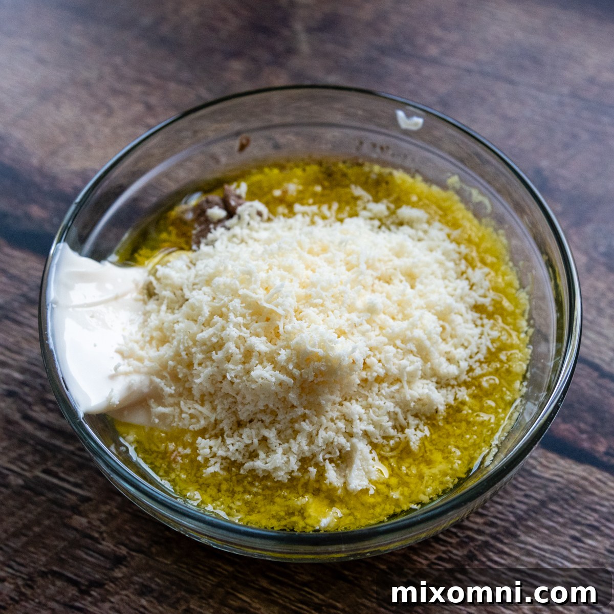 All Caesar dressing ingredients mixed in a clear glass bowl, showcasing its creamy texture.