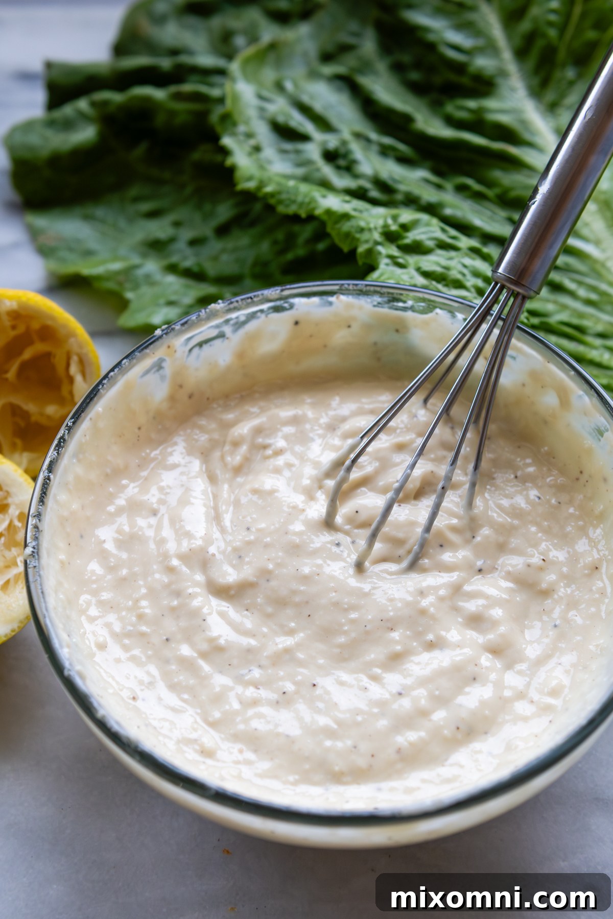A bowl of the creamy homemade Caesar dressing with a whisk, ready to be used.