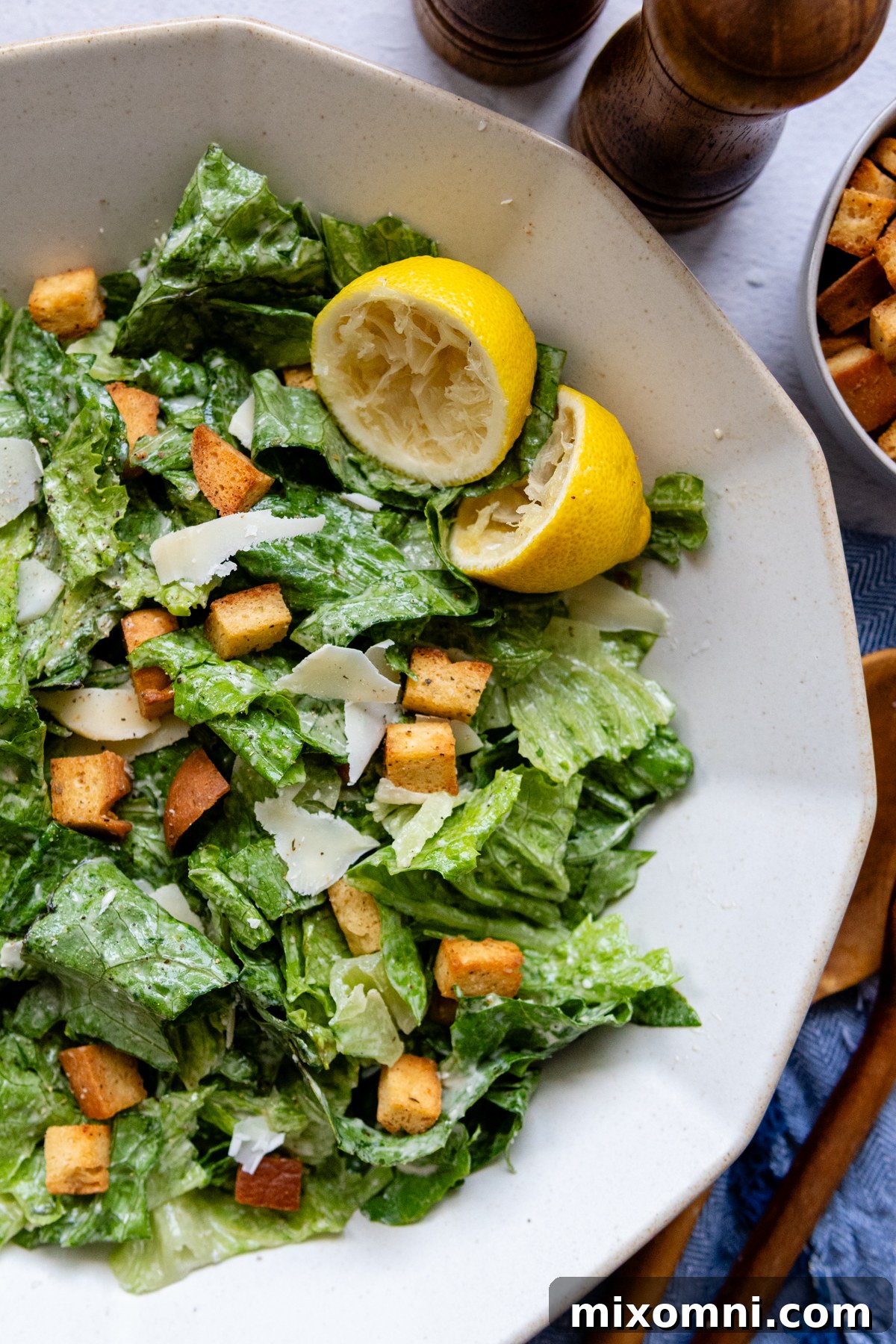 A vibrant Caesar salad in a white bowl, garnished with lemon wedges, ready to serve.