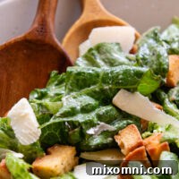 Close up of bowl of Caesar salad with wooden spoons.
