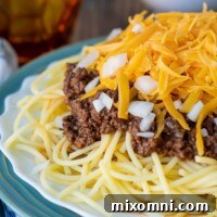 a close up of meat sauce on the pasta with cheese on top and a cup in the background