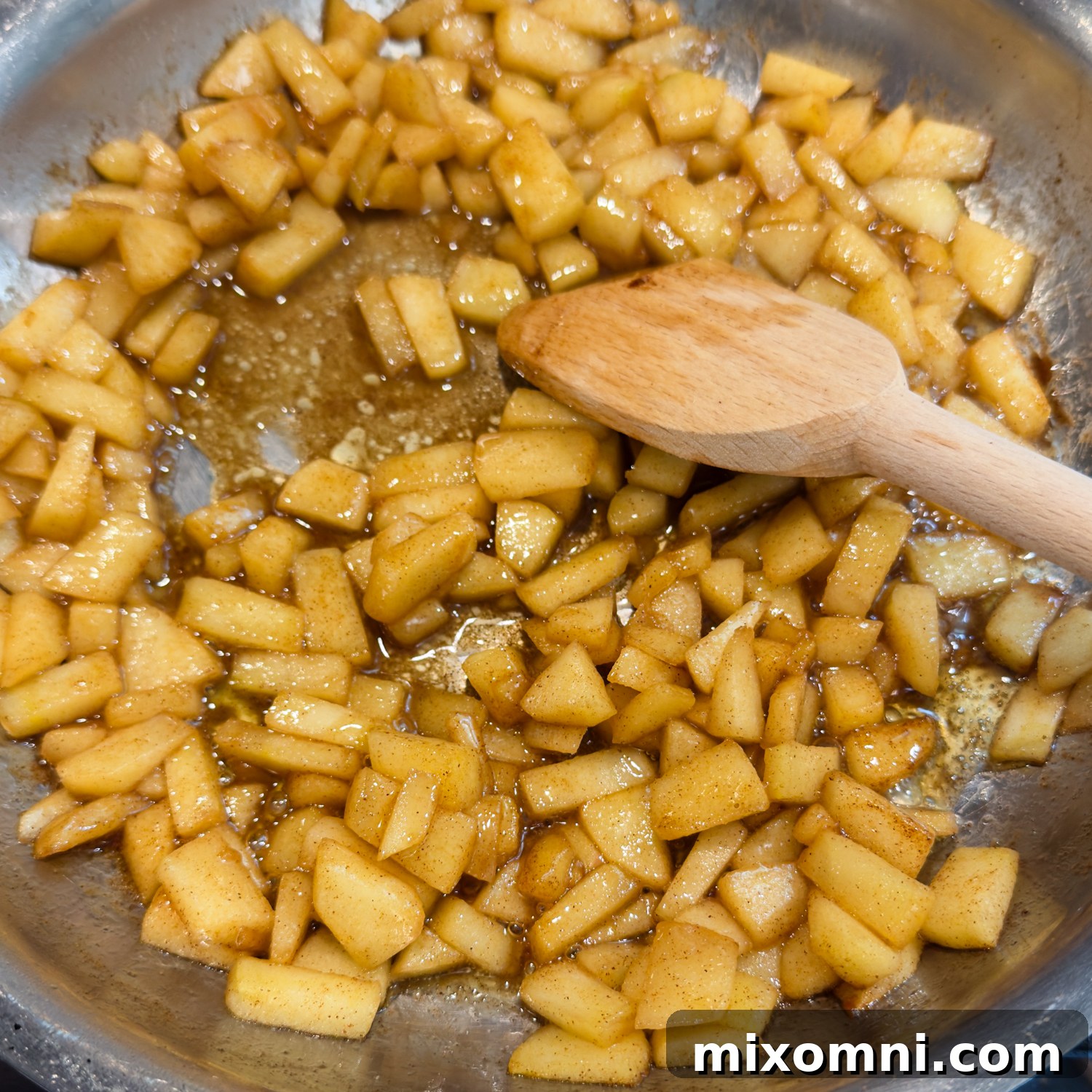 Seasoned apple pieces in a bowl with wooden spoon stirring.