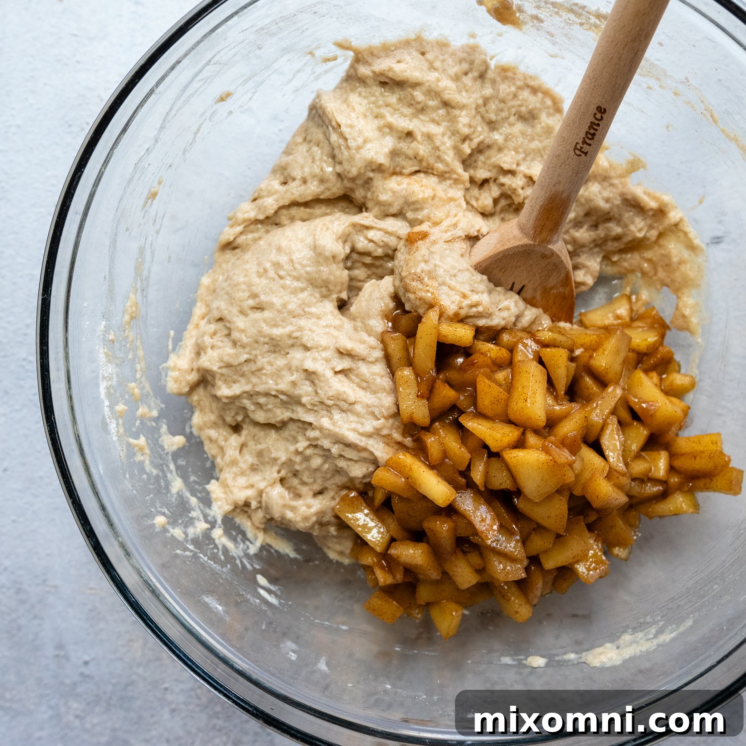Dough and apple pieces in a glass bowl.