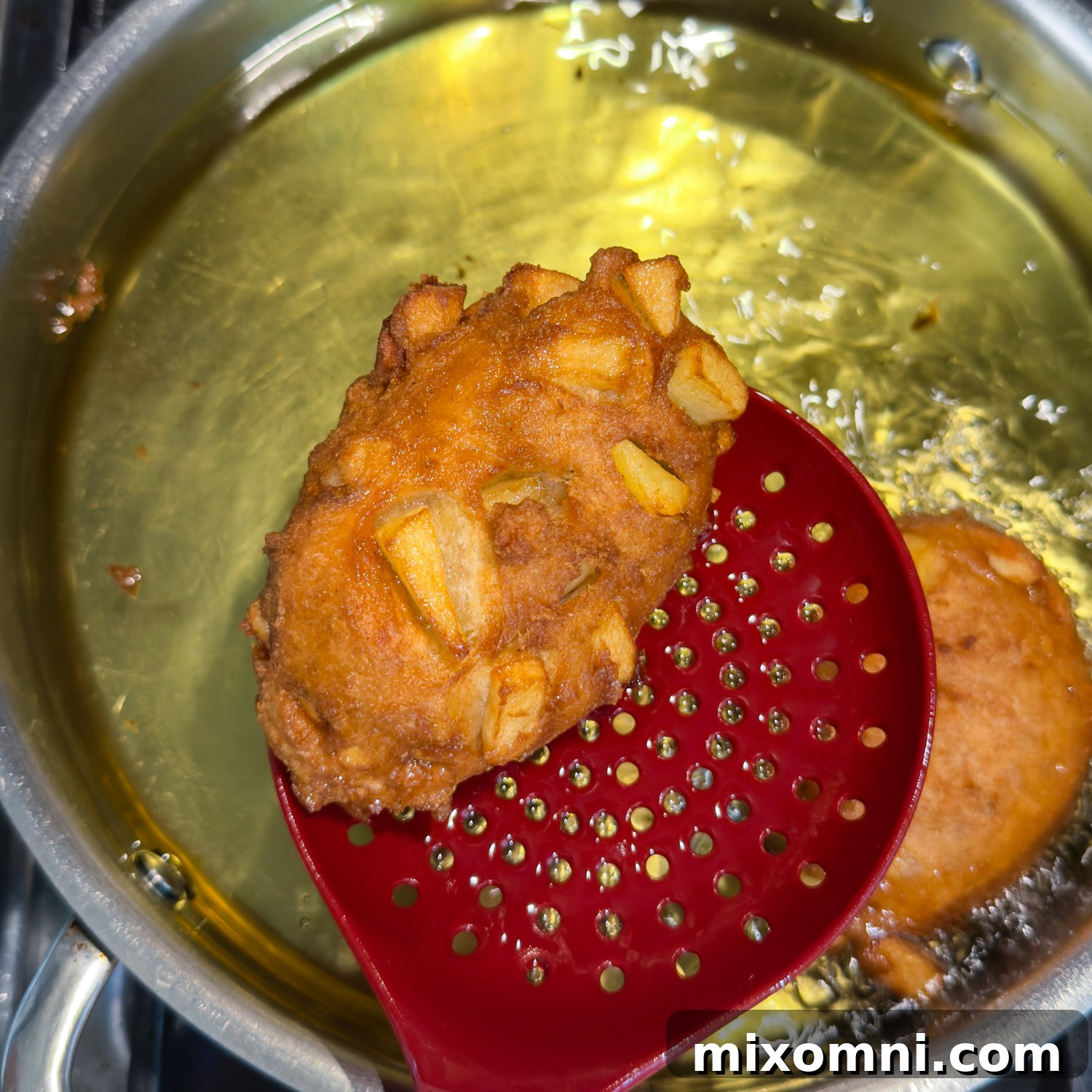 Fritter frying with a red slotted spatula.
