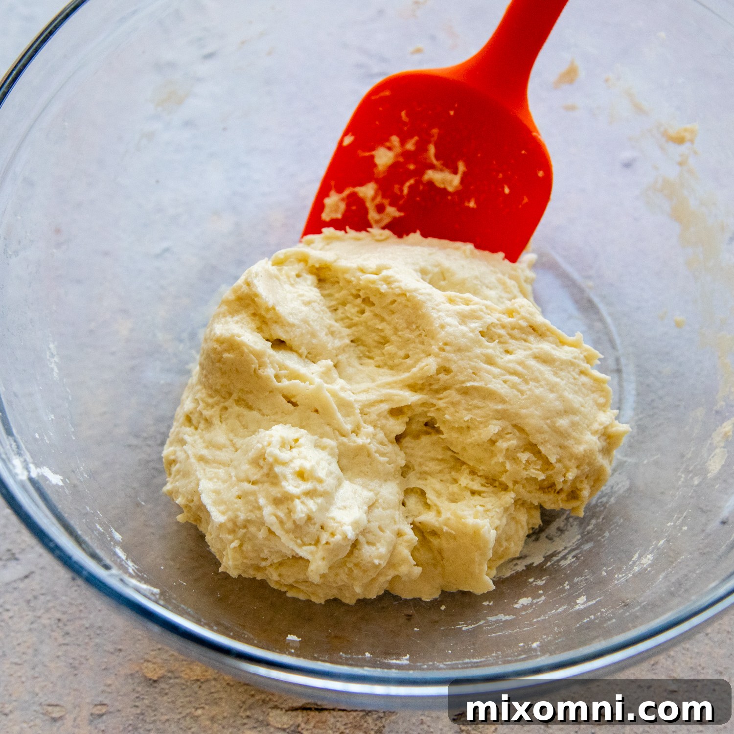 Gluten-free dumpling dough in a glass bowl with a red spatula, ready for cooking.