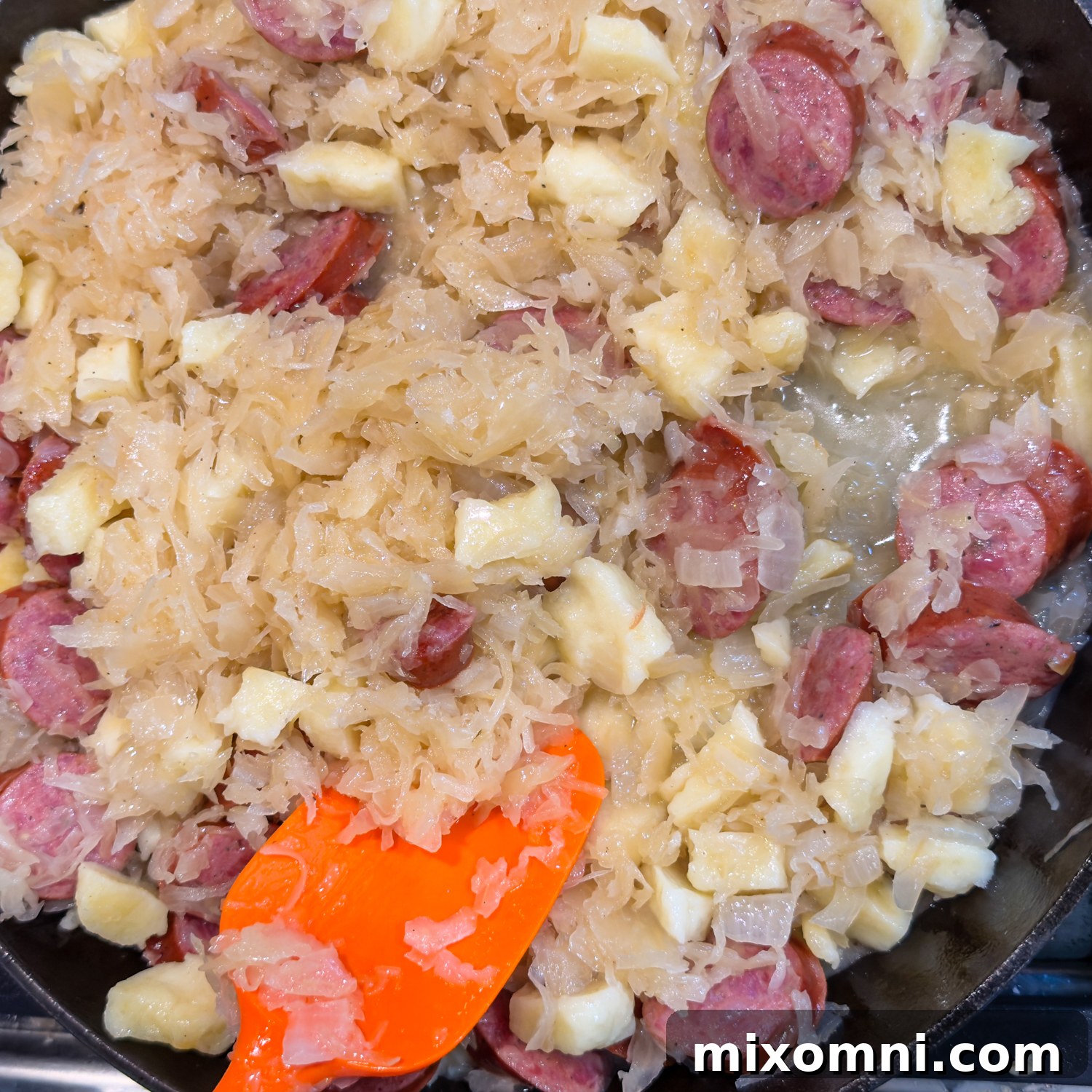 A cast iron skillet filled with savory sauerkraut and browned sausage, actively cooking.