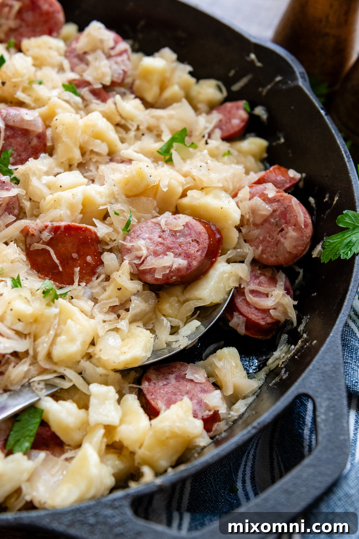 Delicious gluten-free dumplings and sausage mixed with sauerkraut, presented in a cast iron skillet with a serving spoon.