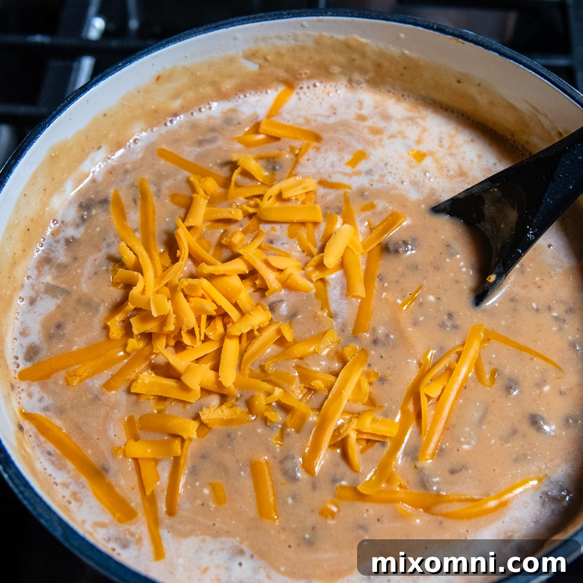 Black spoon mixing in cheese into soup.