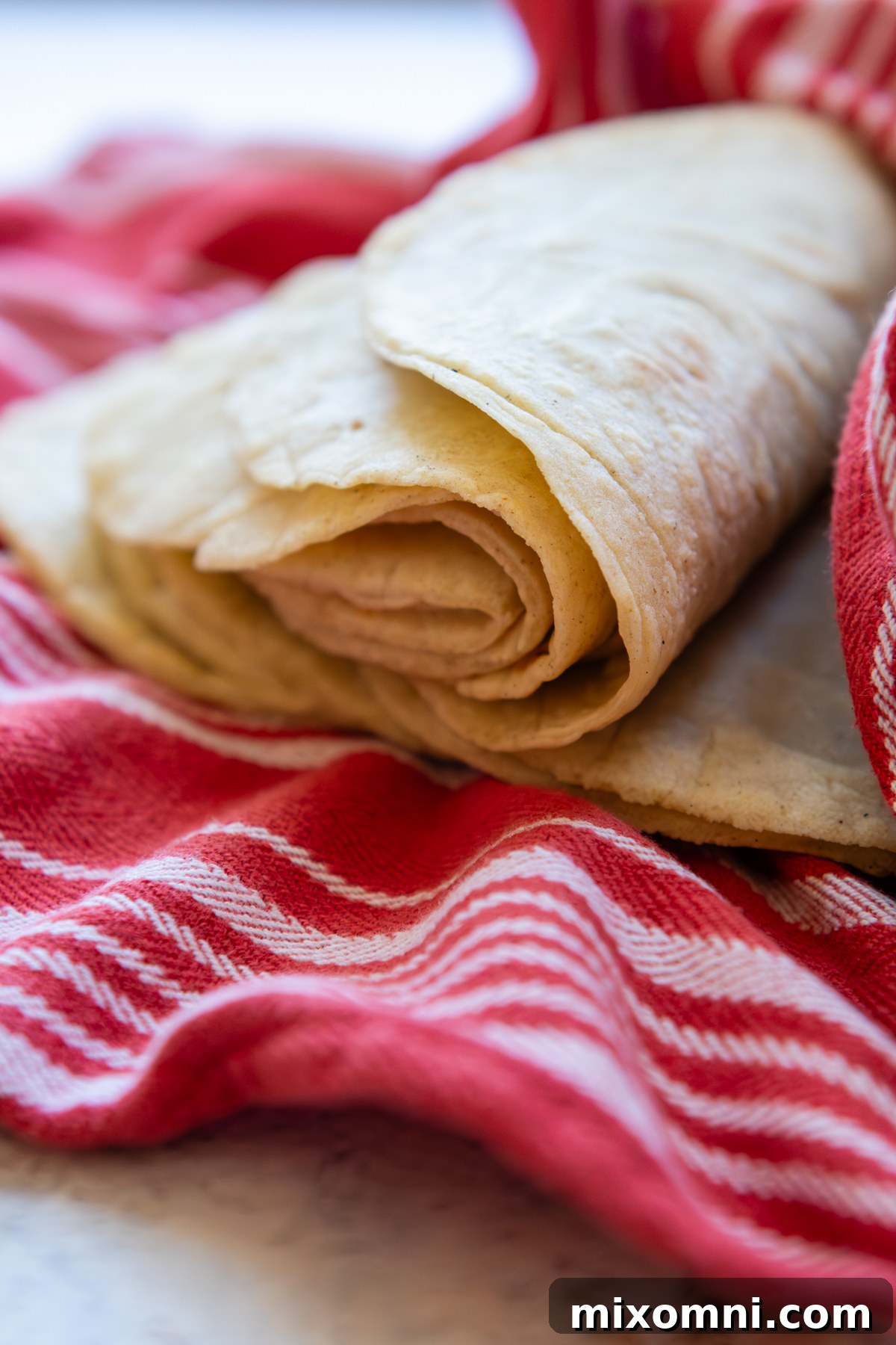 Soft, flexible corn tortillas, folded and resting on a clean kitchen towel.