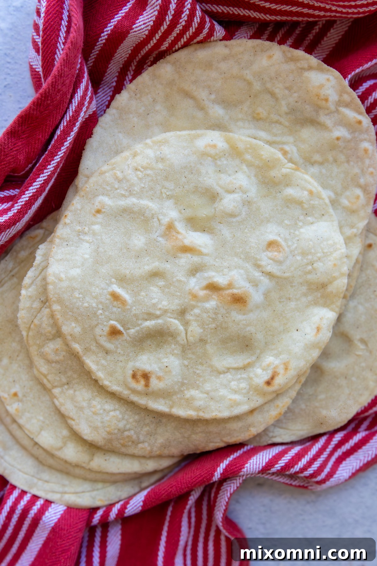 Overhead shot of a stack of golden corn tortillas resting flat on a striped towel, ready to be served.