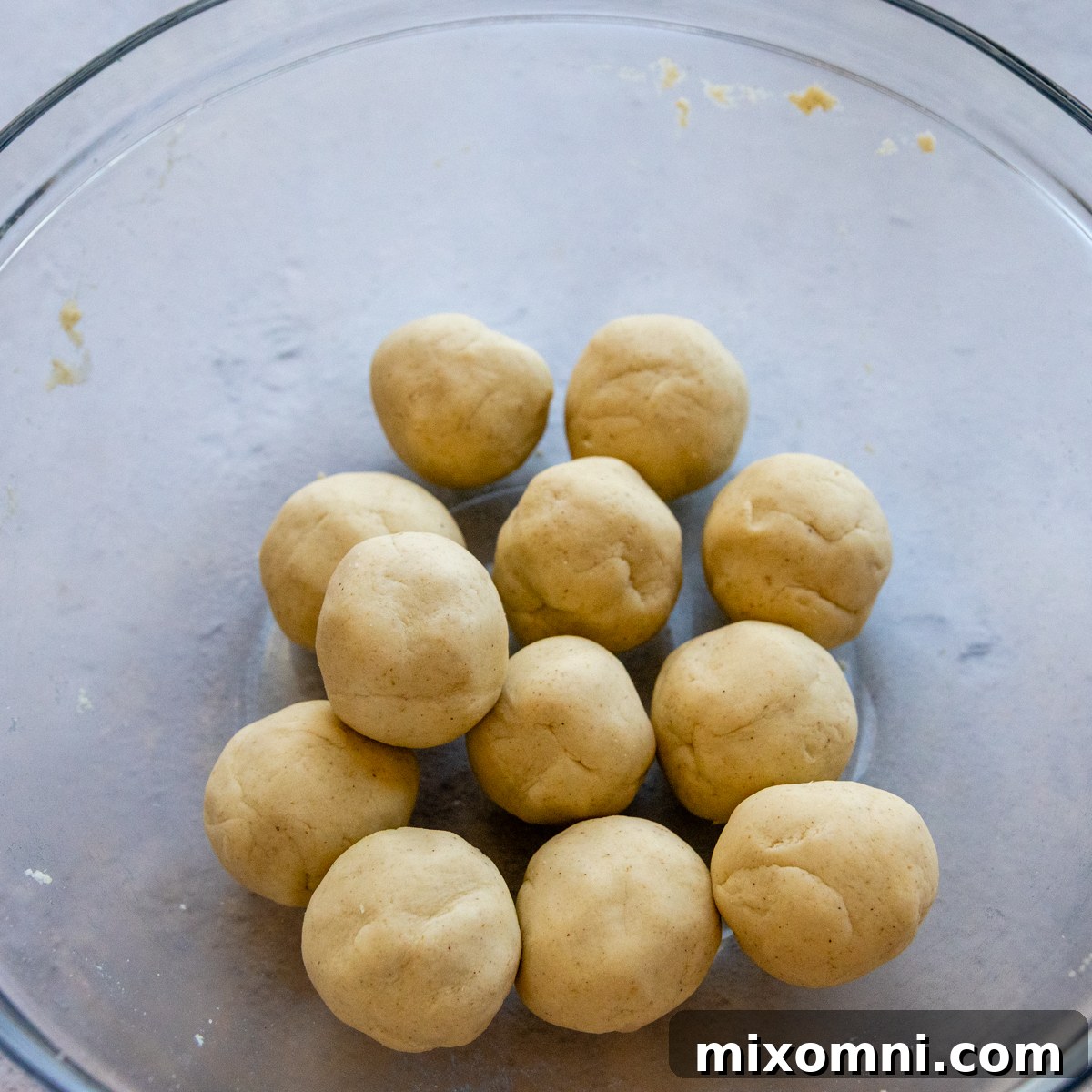 Neatly rolled dough balls covered with plastic wrap in a glass bowl.