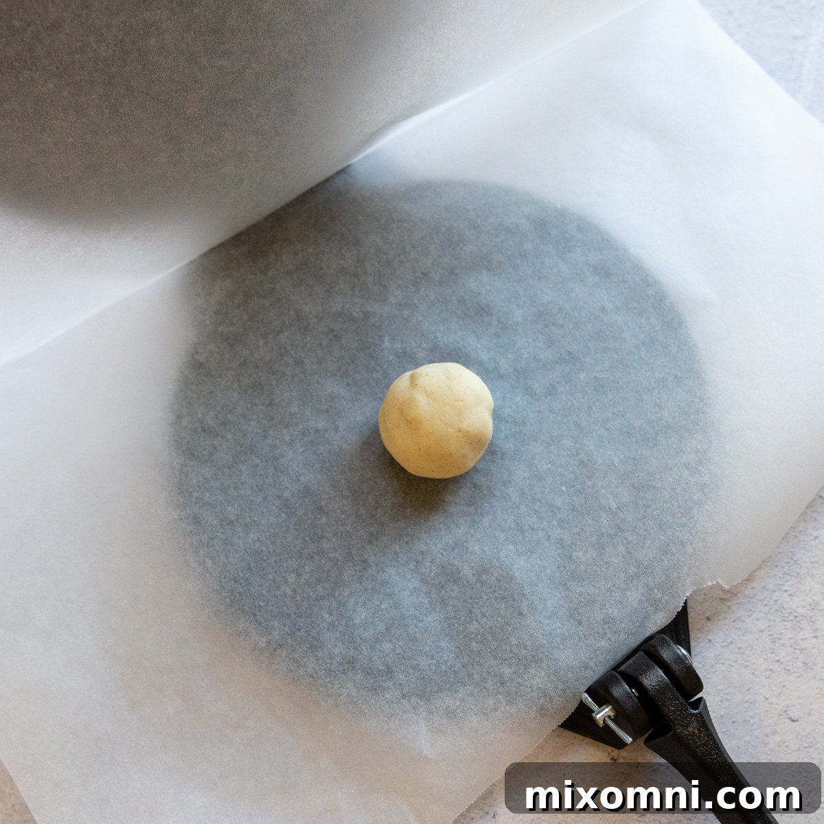A tortilla dough ball placed on parchment paper inside an open tortilla press.