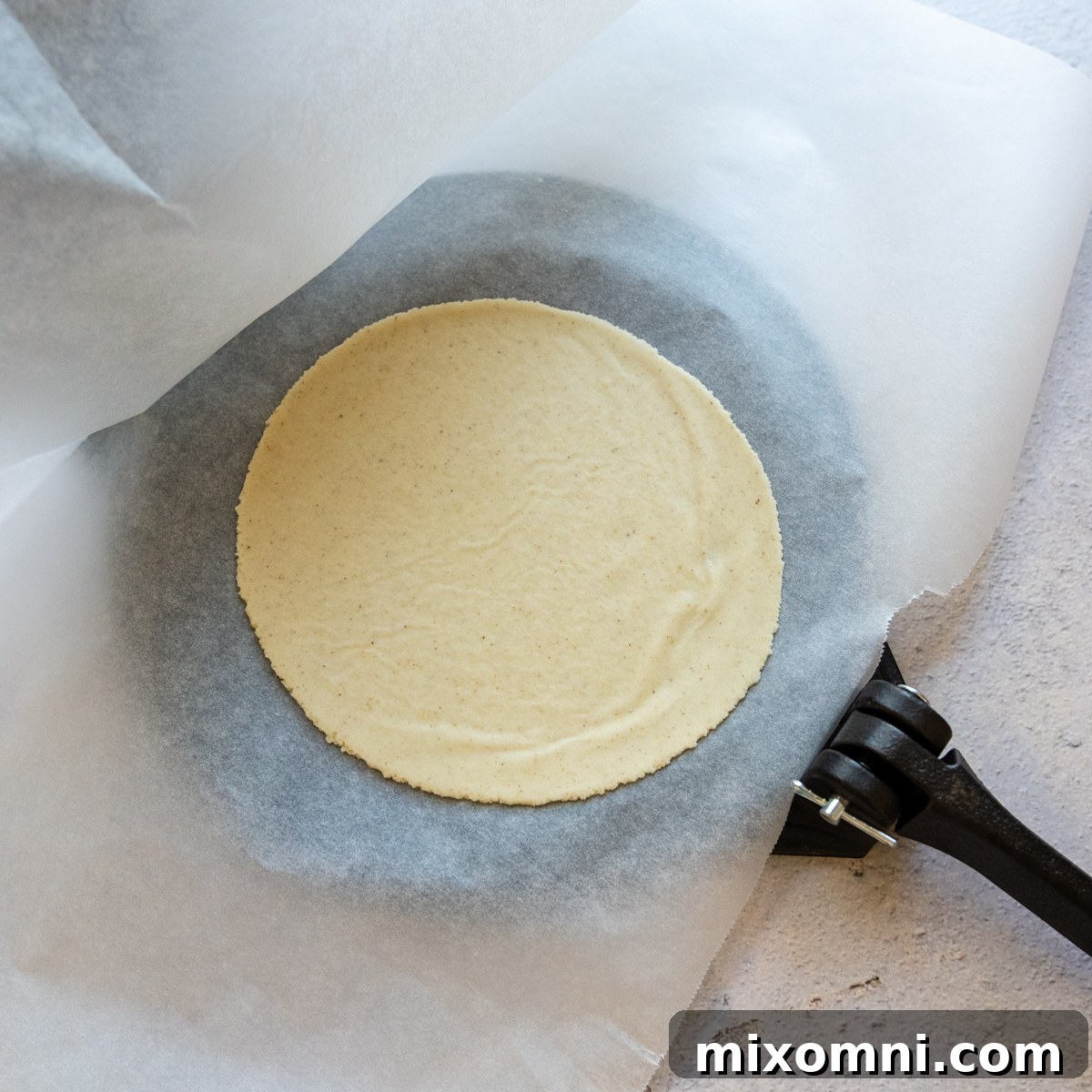 A perfectly flattened tortilla on parchment paper, ready to be cooked.