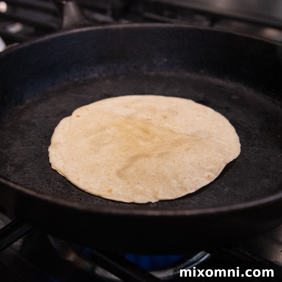 A corn tortilla sizzling and puffing up in a hot cast iron skillet.