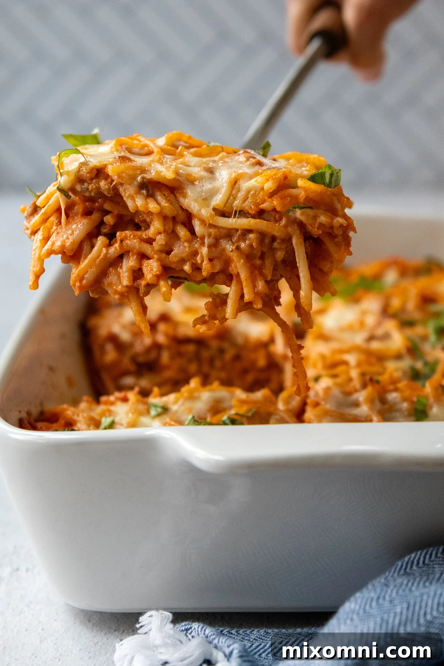 A serving of classic gluten-free baked spaghetti casserole being lifted from a baking dish, showcasing layers of pasta, rich sauce, and melted cheese.