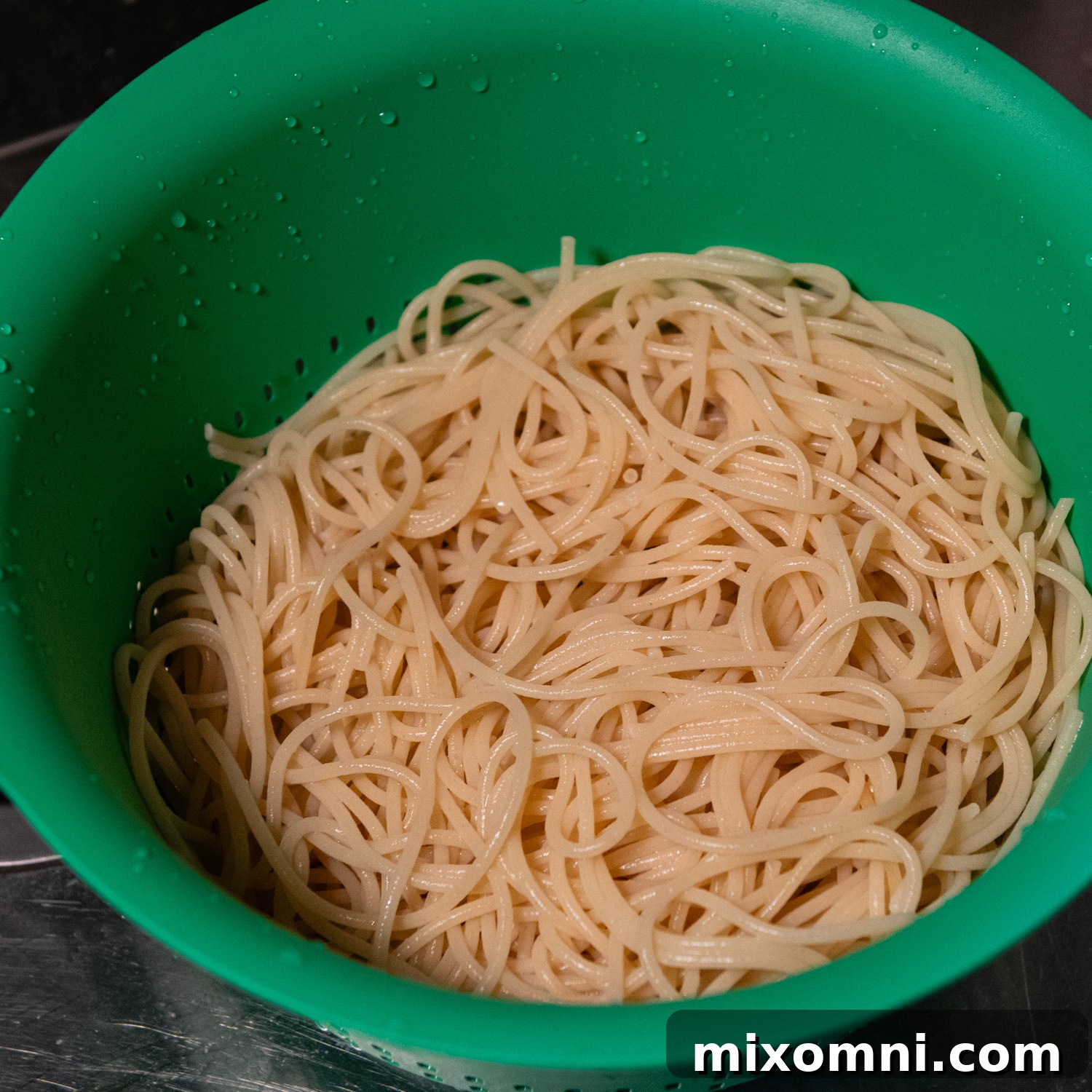 Cooked and rinsed gluten-free spaghetti noodles resting in a vibrant green mixing bowl, perfectly prepared to avoid mushiness.