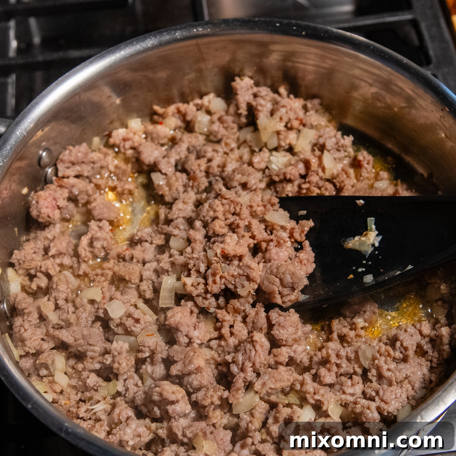 Ground Italian sausage browning in a metal skillet with chopped onions and minced garlic, preparing a flavorful base for the sauce.