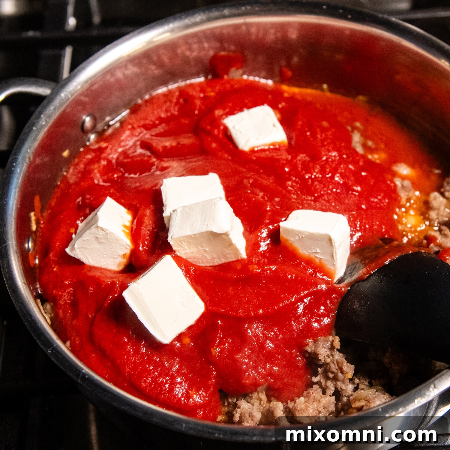 Rich spaghetti sauce simmering in a saucepan, with softened cream cheese melting in to create a creamy texture.