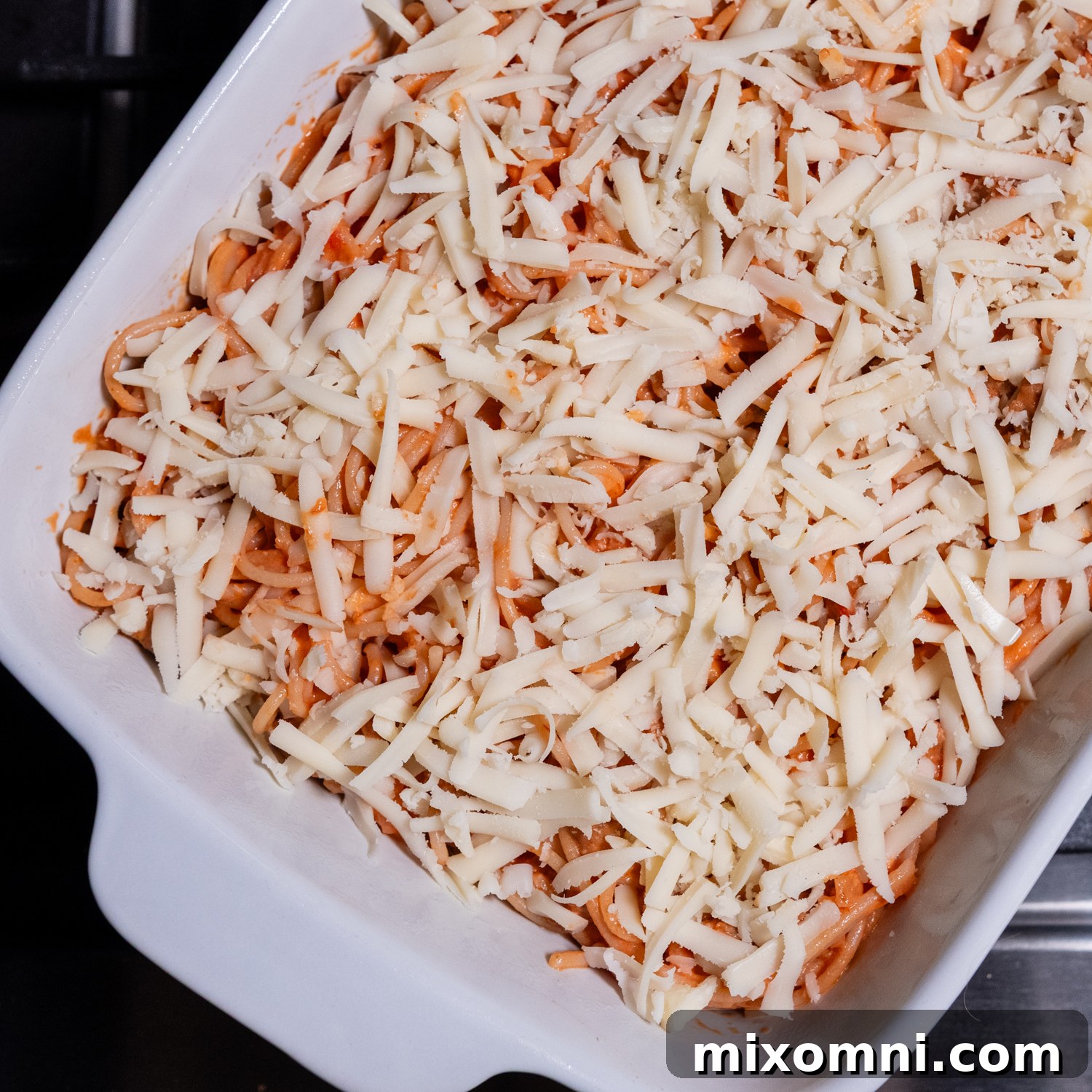 An unbaked gluten-free spaghetti casserole, assembled in a white baking dish and topped with shredded mozzarella cheese, ready for the oven.