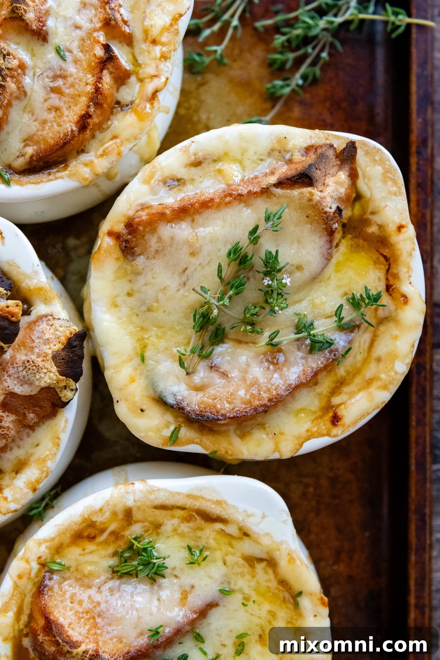 Overhead shot of a beautifully crafted Gluten-Free French Onion Soup in a white ceramic soup crock, garnished with fresh parsley and topped with melted, bubbly Gruyere cheese.