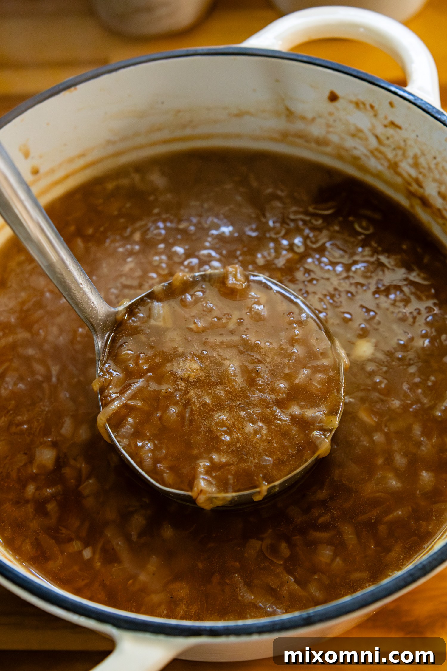 A ladle filled with rich, savory French onion soup hovers over a large pot brimming with the delicious soup, ready to be served into crocks.