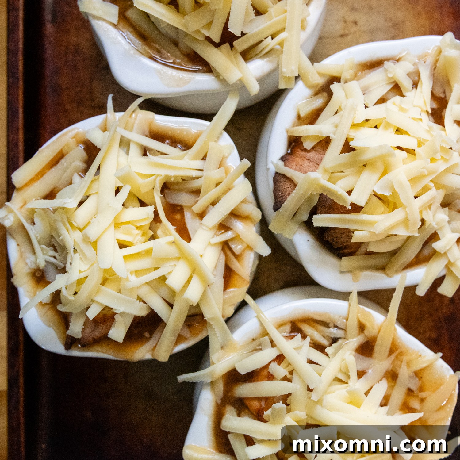 Several soup crocks filled with French onion soup, each topped with toasted gluten-free bread and a generous layer of freshly grated Gruyere cheese, ready for broiling.
