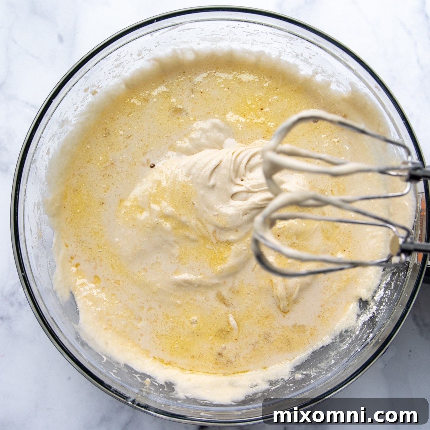 Combined ingredients in glass bowl with beaters hanging over the side.