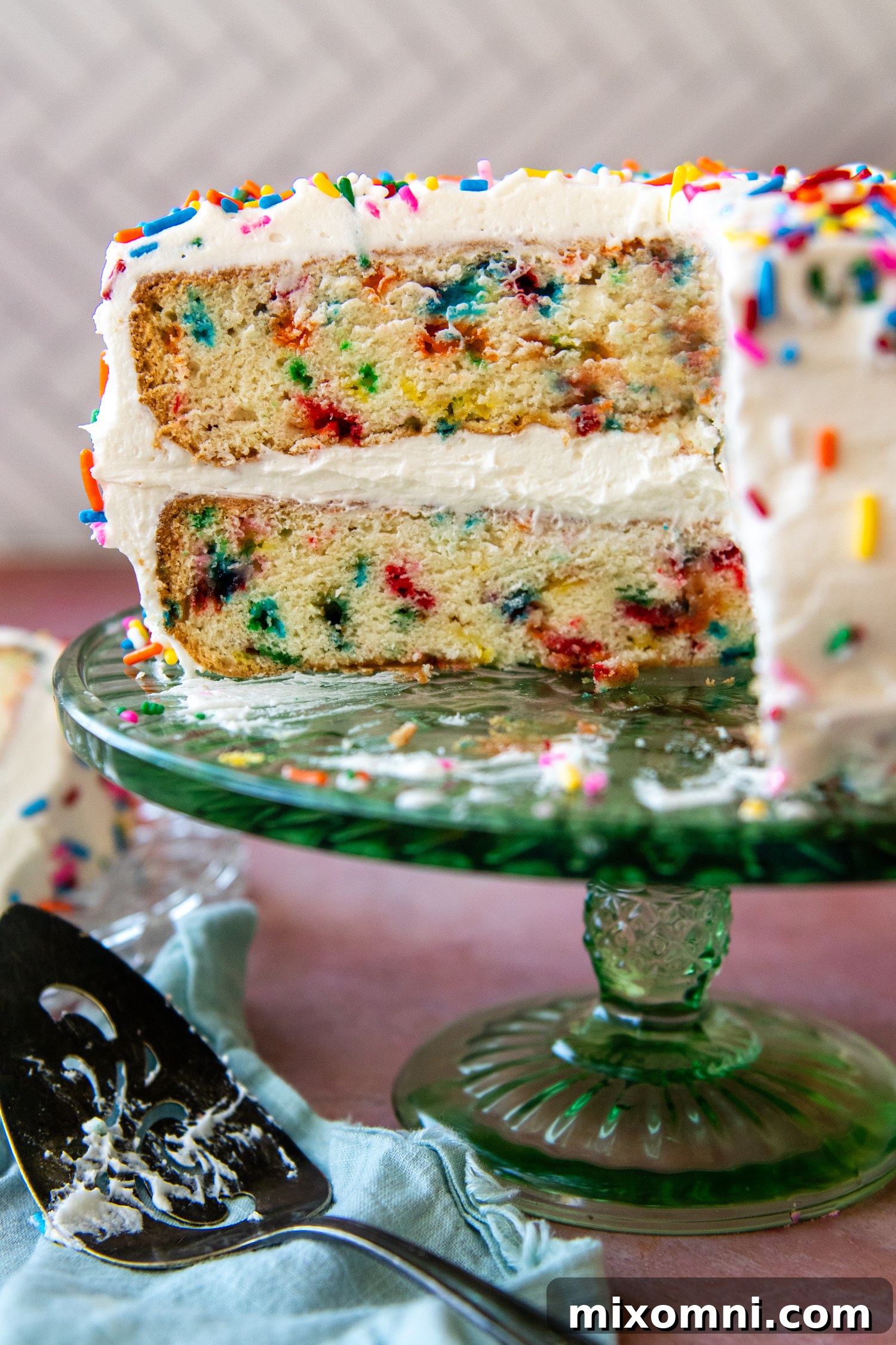 A slice of gluten-free funfetti cake removed from a larger cake on a glass cake stand, showing its moist interior and sprinkles.