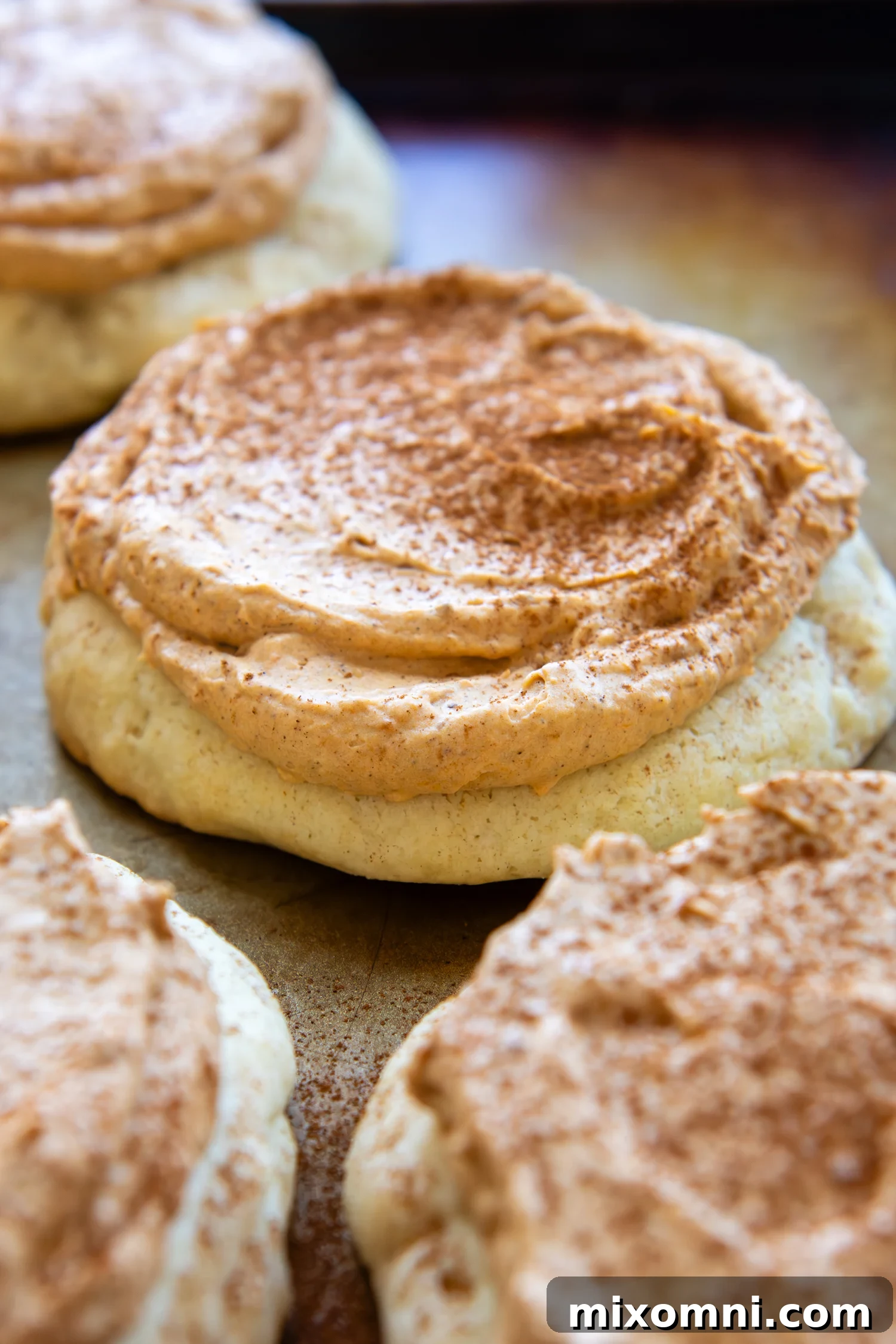 Thick, soft gluten-free pumpkin cream pie cookies topped with fluffy pumpkin spice frosting on a cooling rack, ready to be devoured.
