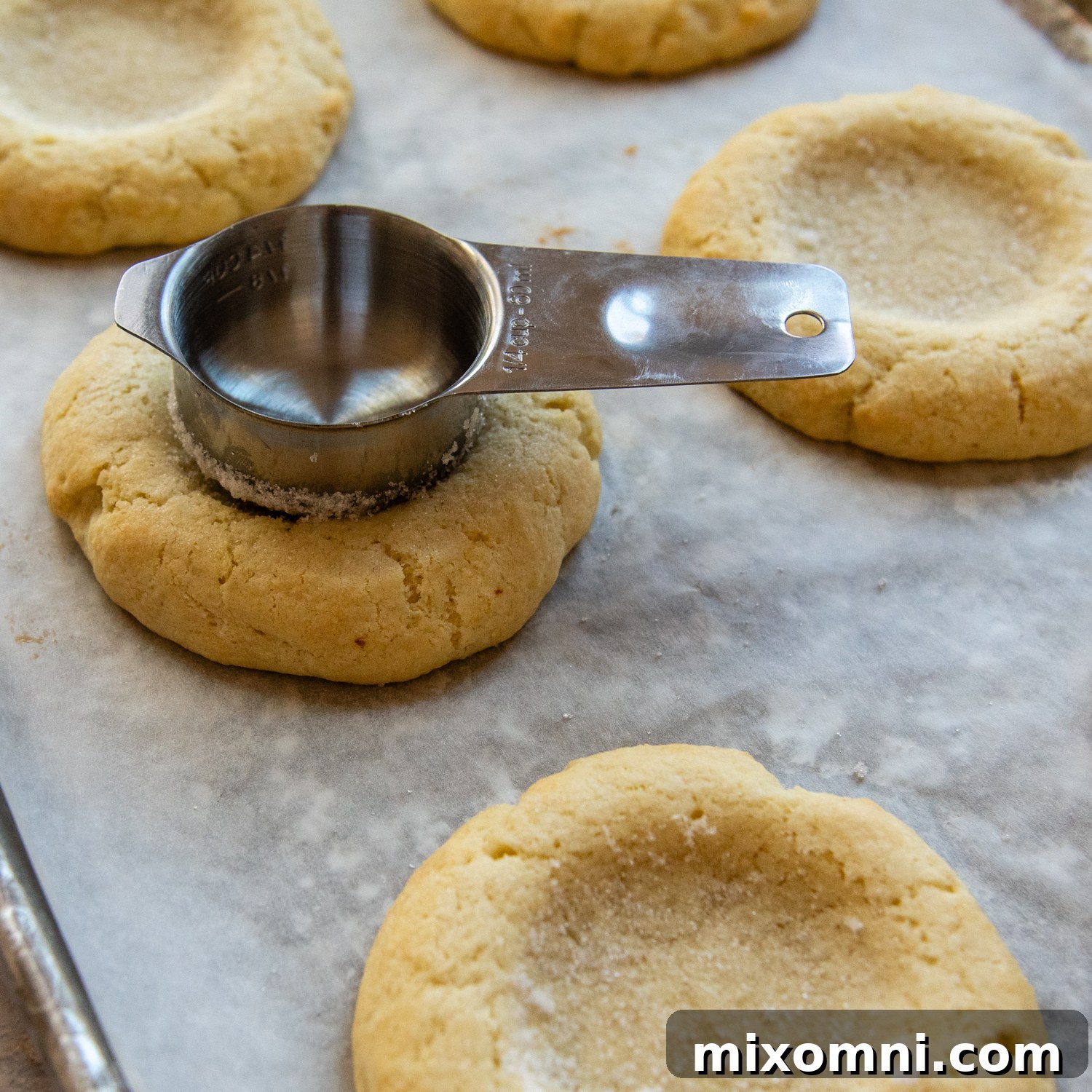 A measuring cup being gently pressed into the center of a baked and cooled cookie to redefine the well for frosting.