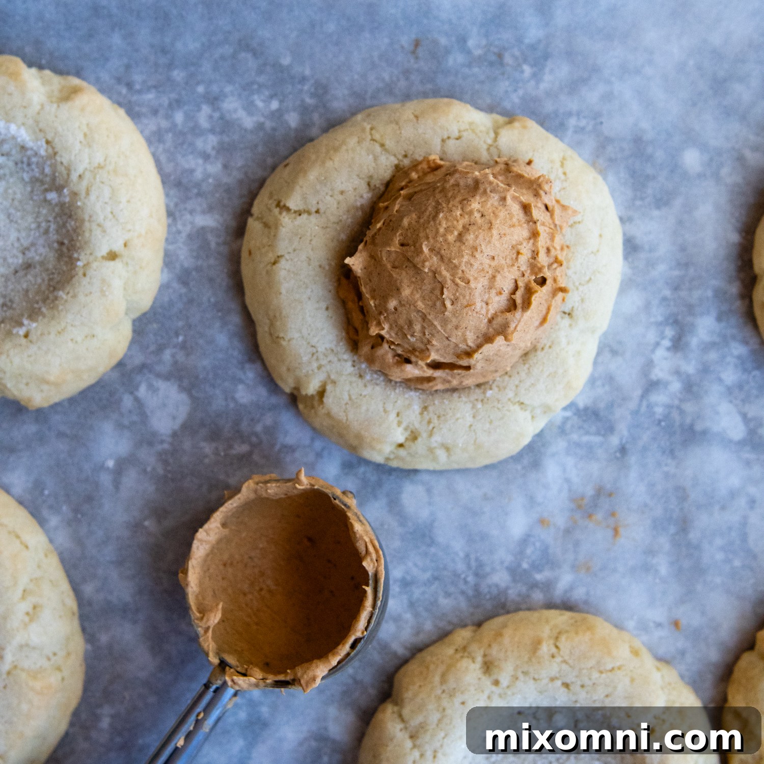 A generous scoop of fluffy pumpkin cream frosting being added to the center of a cooled gluten-free sugar cookie.