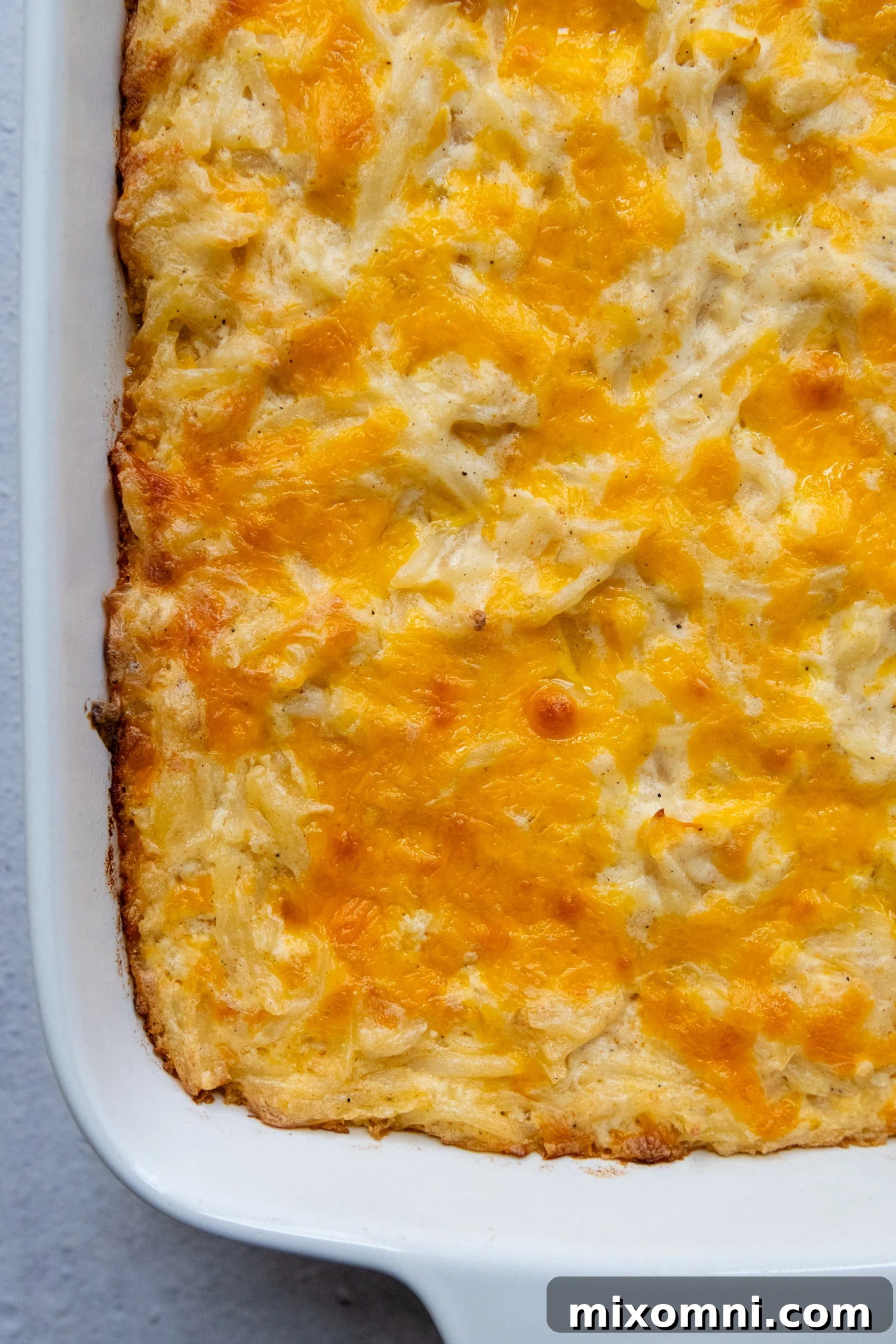 Golden brown cheesy gluten-free hash brown casserole in a white baking dish.