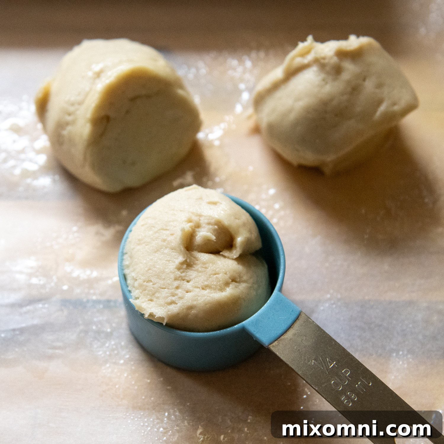 A portion of sticky gluten-free Hawaiian roll dough being scooped out of a mixing bowl with a greased measuring spoon, illustrating the hands-on shaping technique.