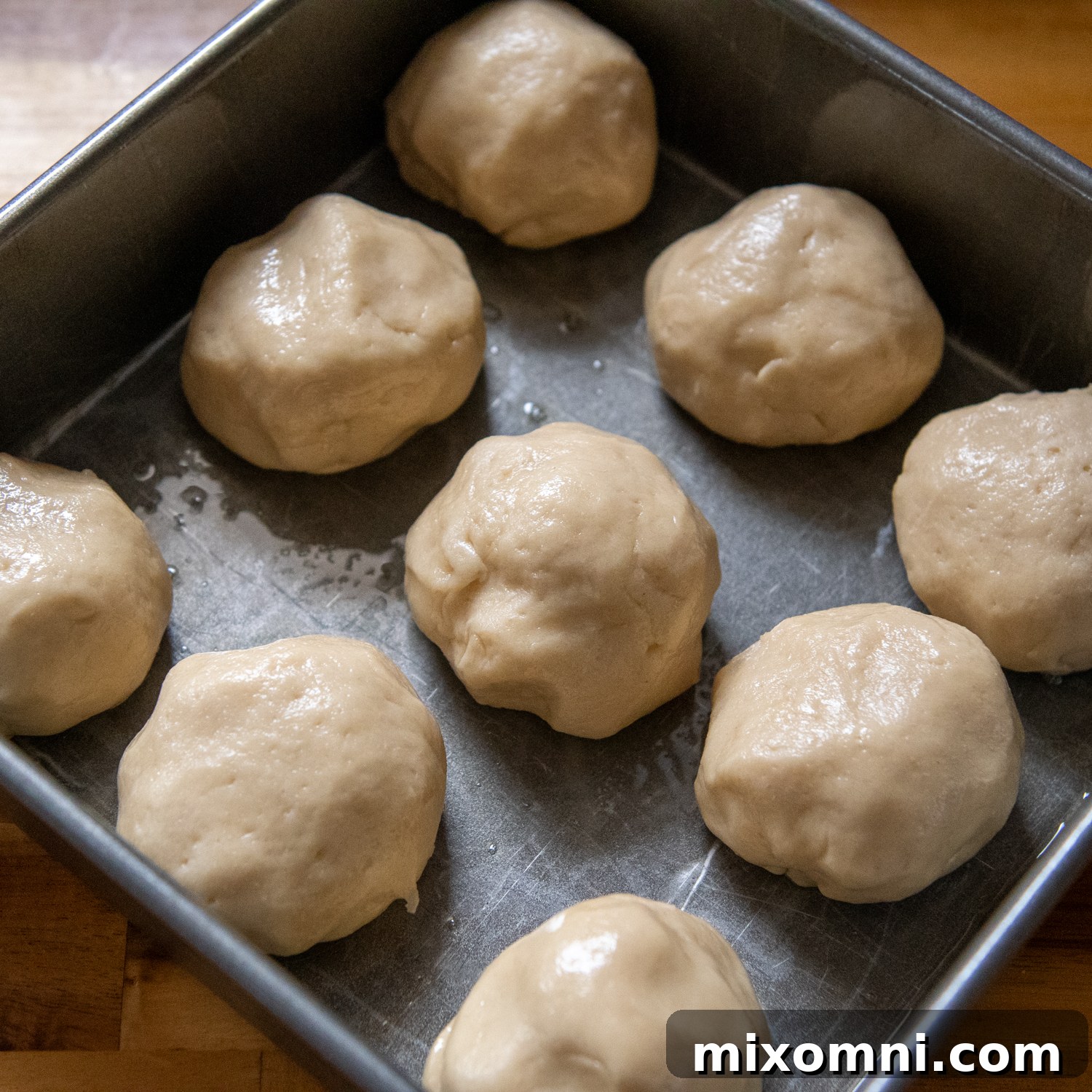 Freshly shaped gluten-free Hawaiian roll dough balls, arranged neatly in an 8x8 inch baking pan, before rising, showcasing their initial compact form.