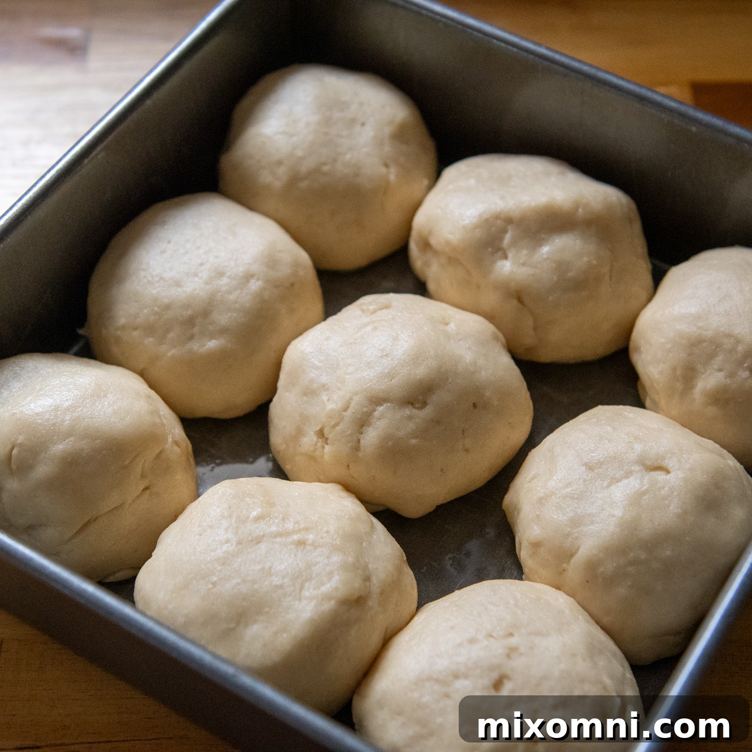 Gluten-free Hawaiian roll dough balls, visibly larger and softer after their first rise in a baking pan, showing the successful yeast activation.