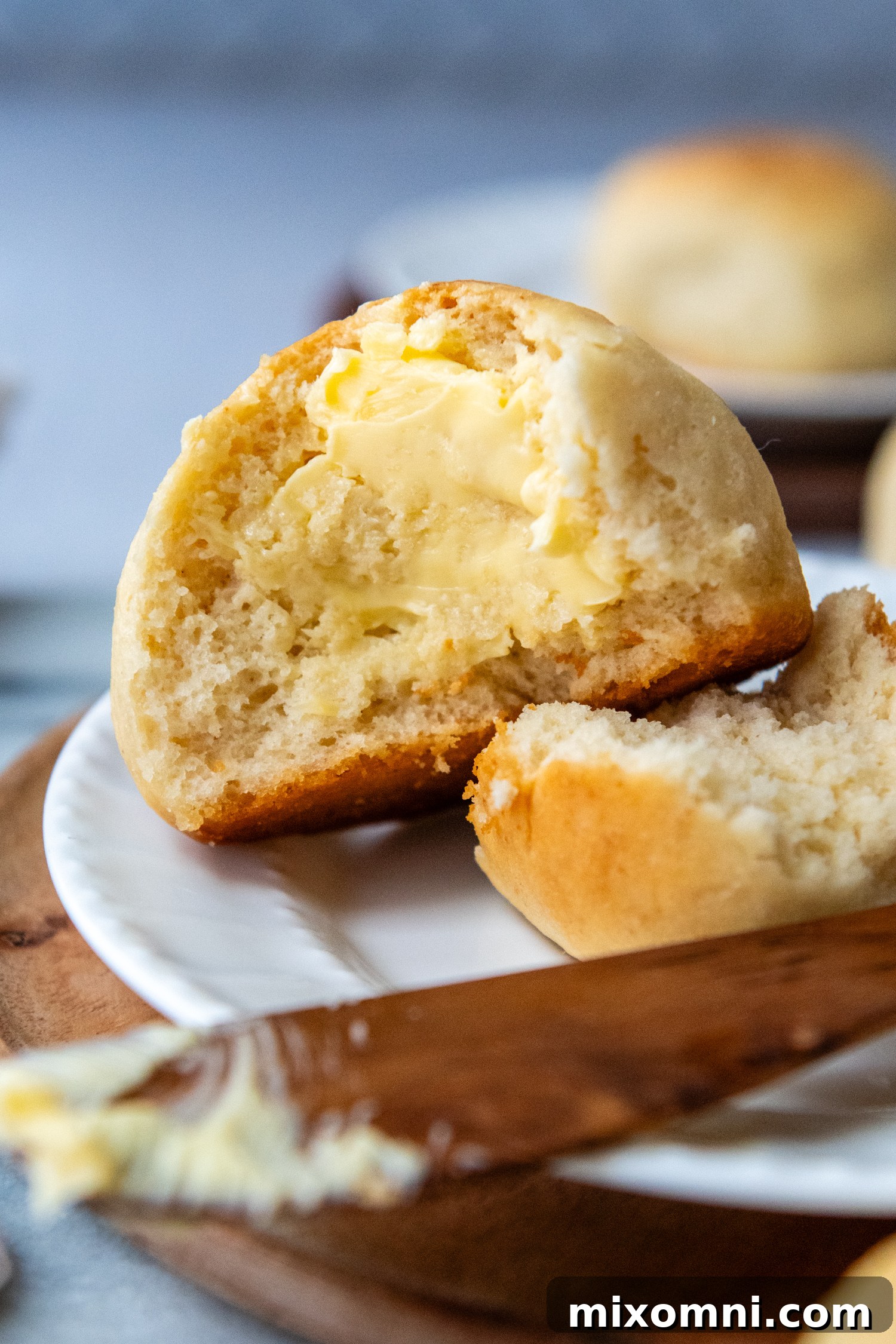 A freshly baked, soft gluten-free Hawaiian roll torn open, revealing its airy interior, with a dollop of melted butter on top, ready to be enjoyed.