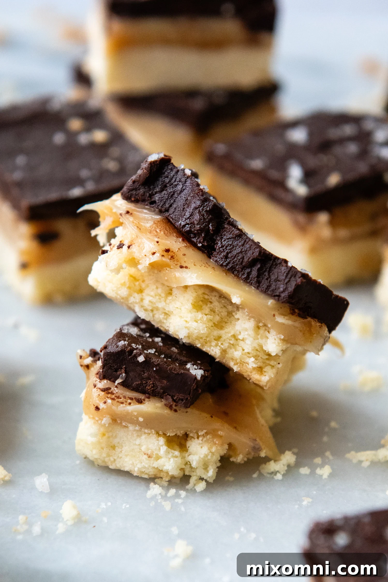 Stack of gluten free millionaire bars with a bite taken from the top one, showcasing the shortbread, caramel, and chocolate layers.