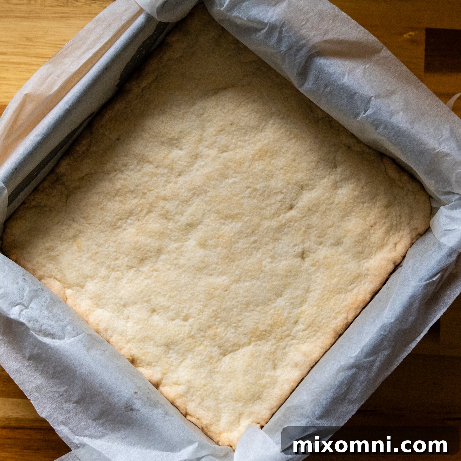 Baked shortbread crust cooling in a metal baking pan lined with parchment paper.
