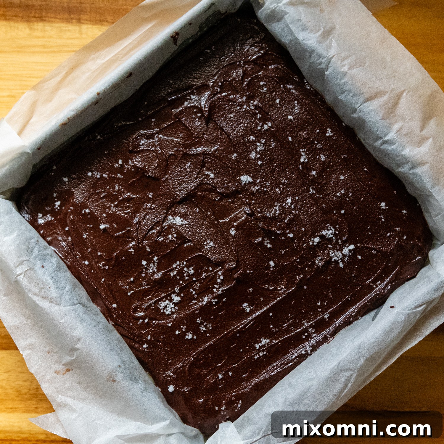 Chocolate topping with flaky sea salt sprinkled on top, covering the caramel layer in a pan.