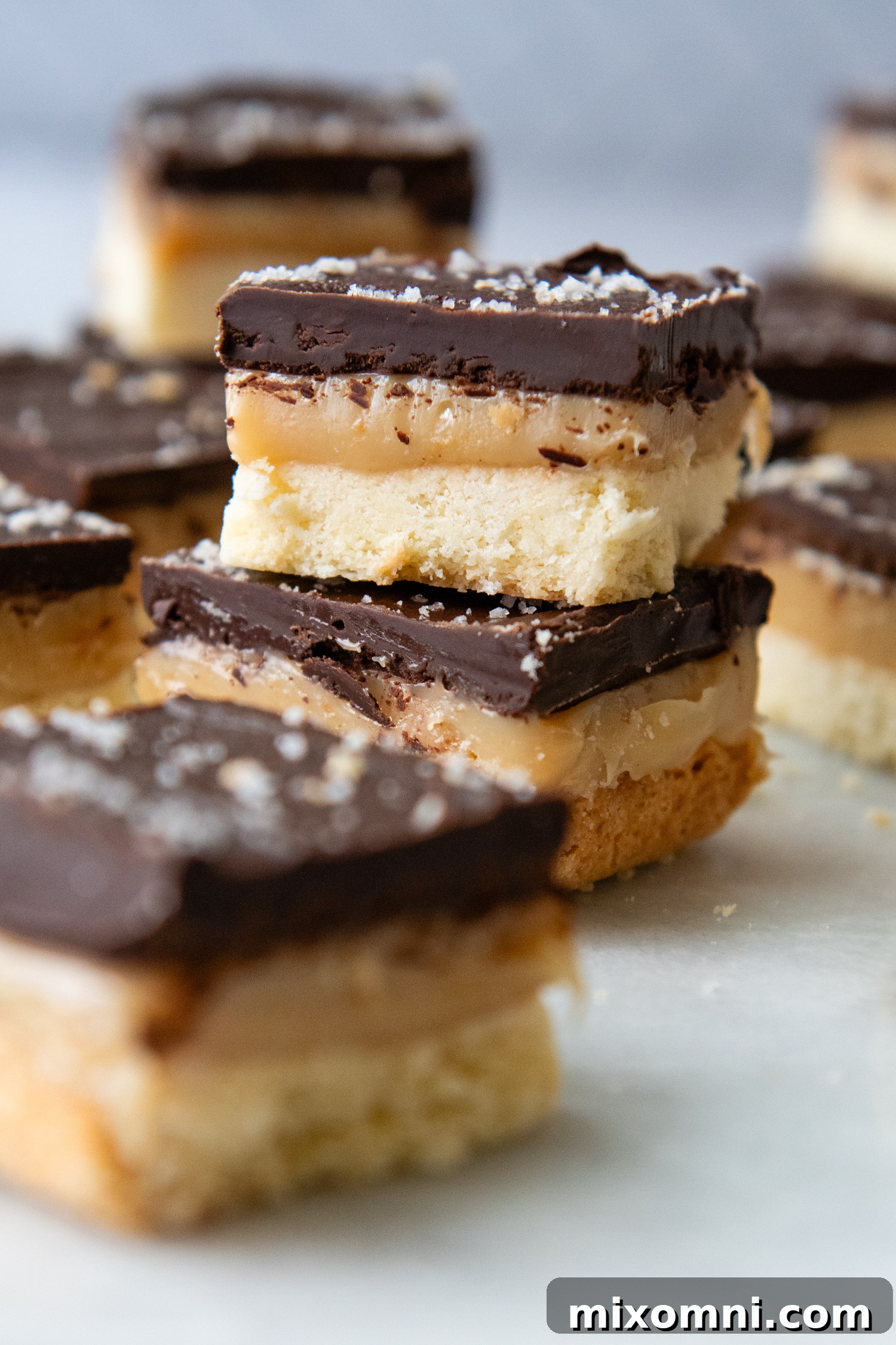 Neatly cut gluten free millionaire bars stacked on a serving plate, showing off the distinct layers.