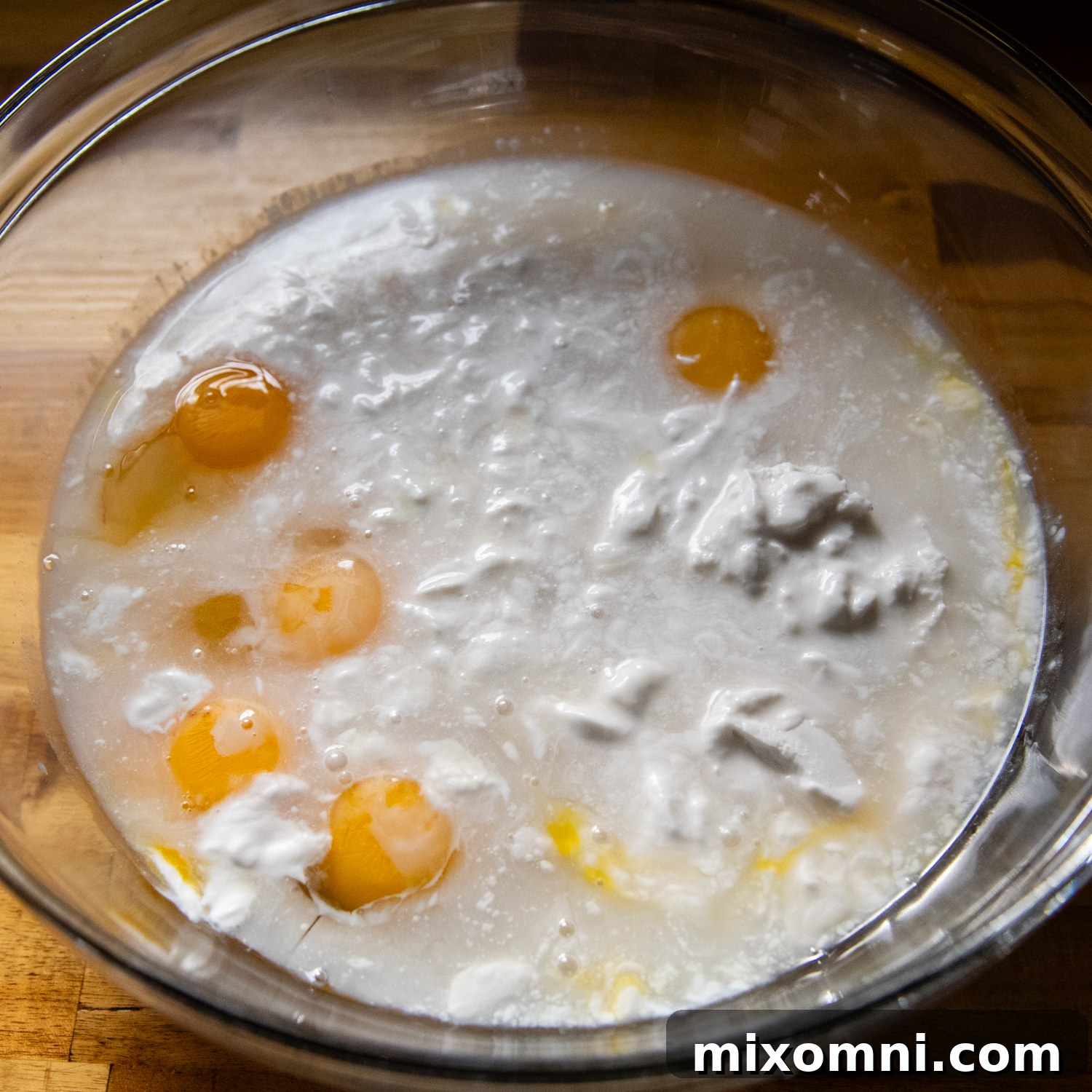 A smooth, pale liquid flan mixture, comprised of coconut milk, sweetened condensed milk, and eggs, in a clear glass mixing bowl, ready for the toasted coconut.